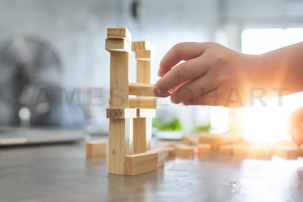 
Hand Of Kid Playing A Blocks Wood Tower Game Of Architectural Project With Sun Flare And Blur Background