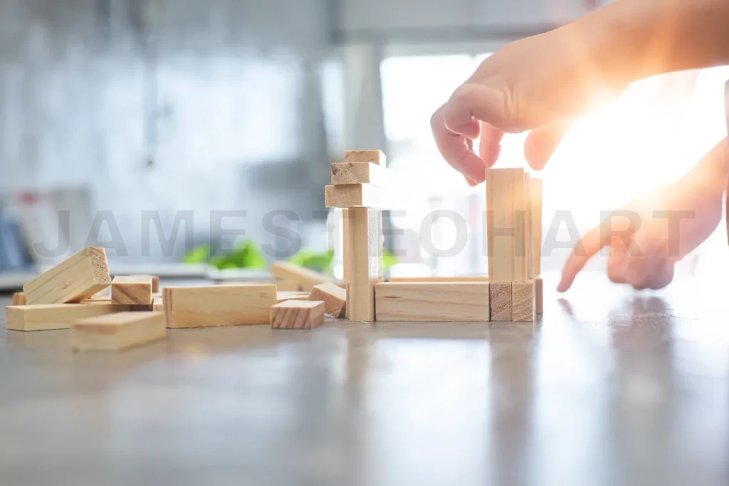 
Hand Of Kid Playing A Blocks Wood Tower Game Of Architectural Project With Sun Flare And Blur Background