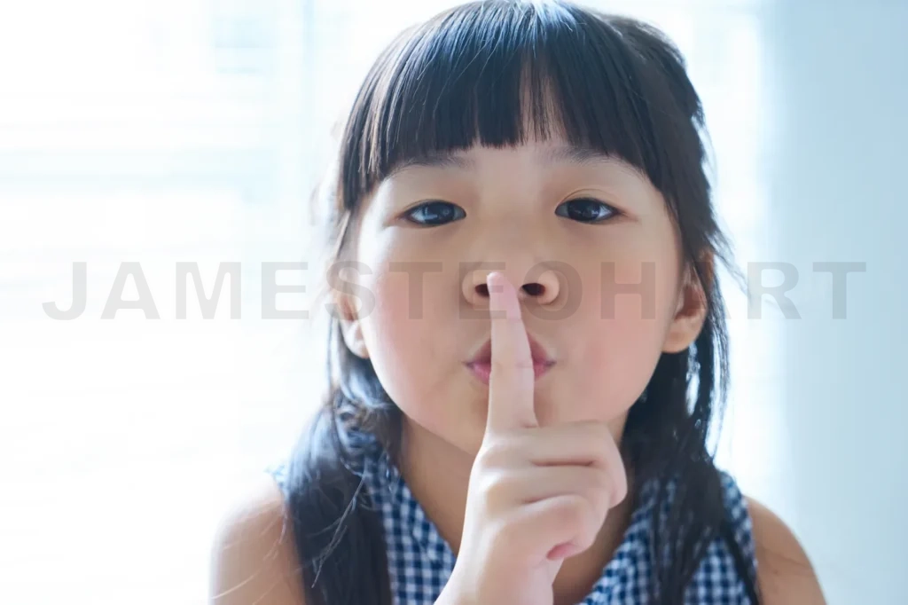 
Closeup Portrait Of Little Asian Chinese Girl Holding Her Finger To Her Lips In A Gesture For Silence