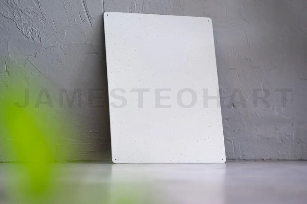 
White blank metal plate leaning on gray wall with green blurred foreground