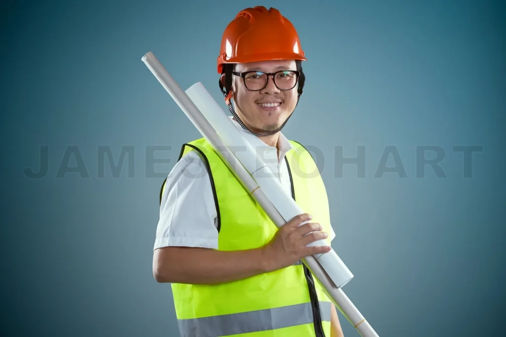 
Young Asian Construction Workers In Safety Helmet And Hold The Rolled Blueprints, Isolated On Blue Background