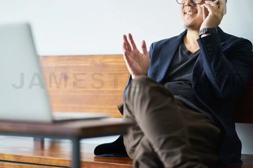 
Businessman Sit On Wooden Chair Using Smartphone In Front Of The Laptop