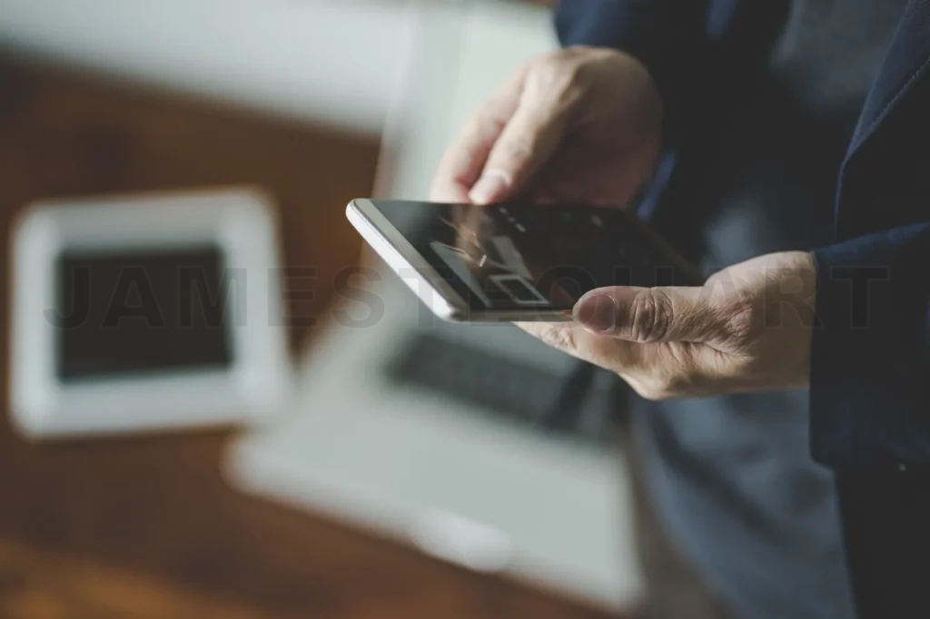 
Top Angle And Closeup View  Of Businessman Using The Smartphone With Blur Laptop And Digital Pad Background