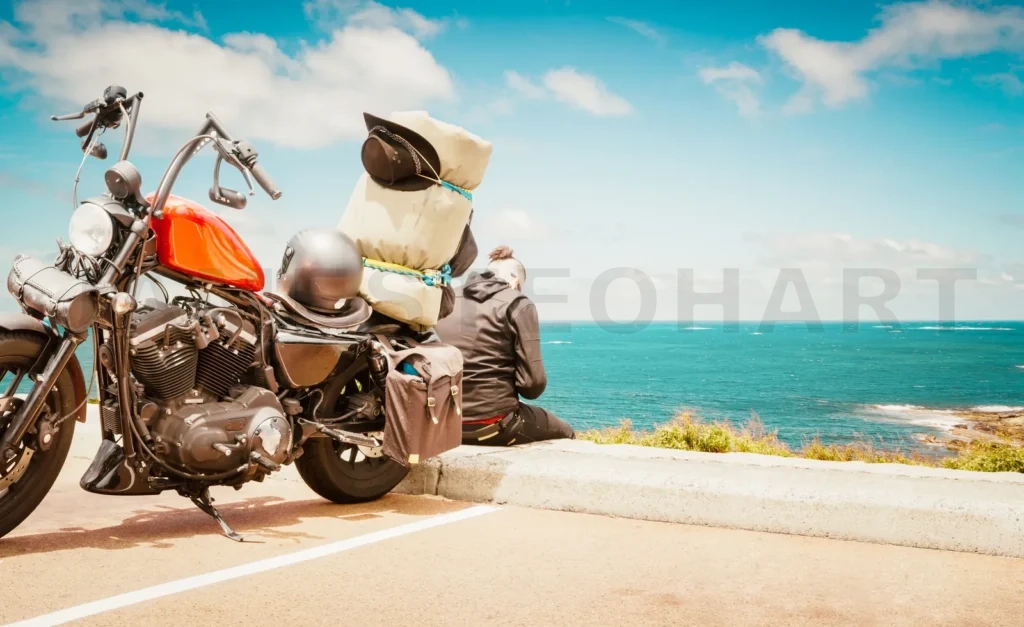 
Biker Man Wearing A Leather Jacket And Sunglasses Sitting On His Vintage Motorcycle Back With A Beautiful Landscape