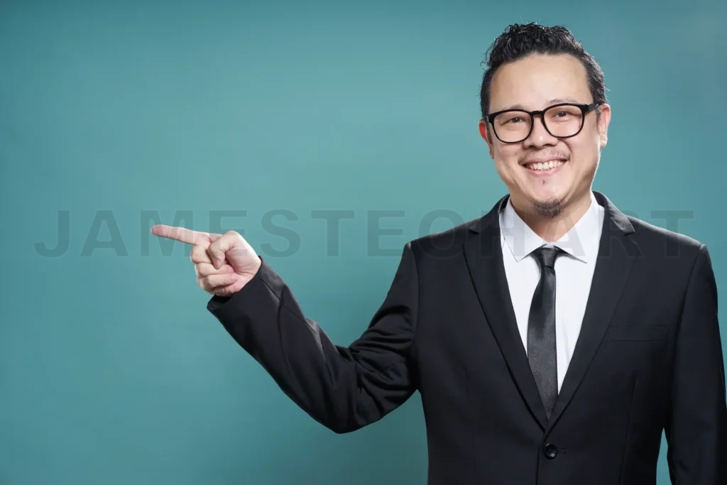 
Portrait Of Asian Businessman Smile And Points With Finger To Camera Left On Vintage Blue Background