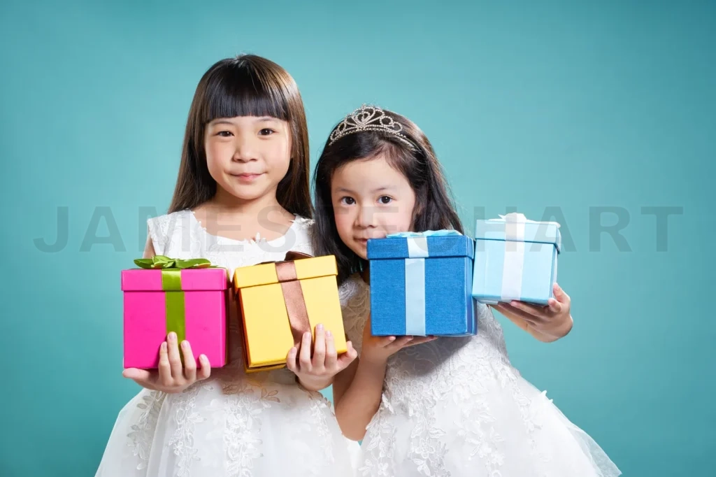 
Portrait Of Two Little Asian Girls Holding Birthday Presents ,  Isolated On Light Blue Background