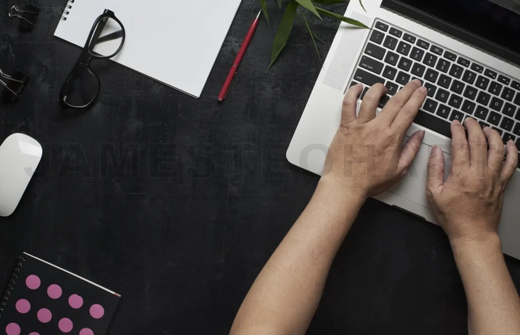 
Workspace With Laptop, Male Hands, Notebook,Eyeglasses, Sketchbook, Black Wooden Desk With Bamboo Leaf