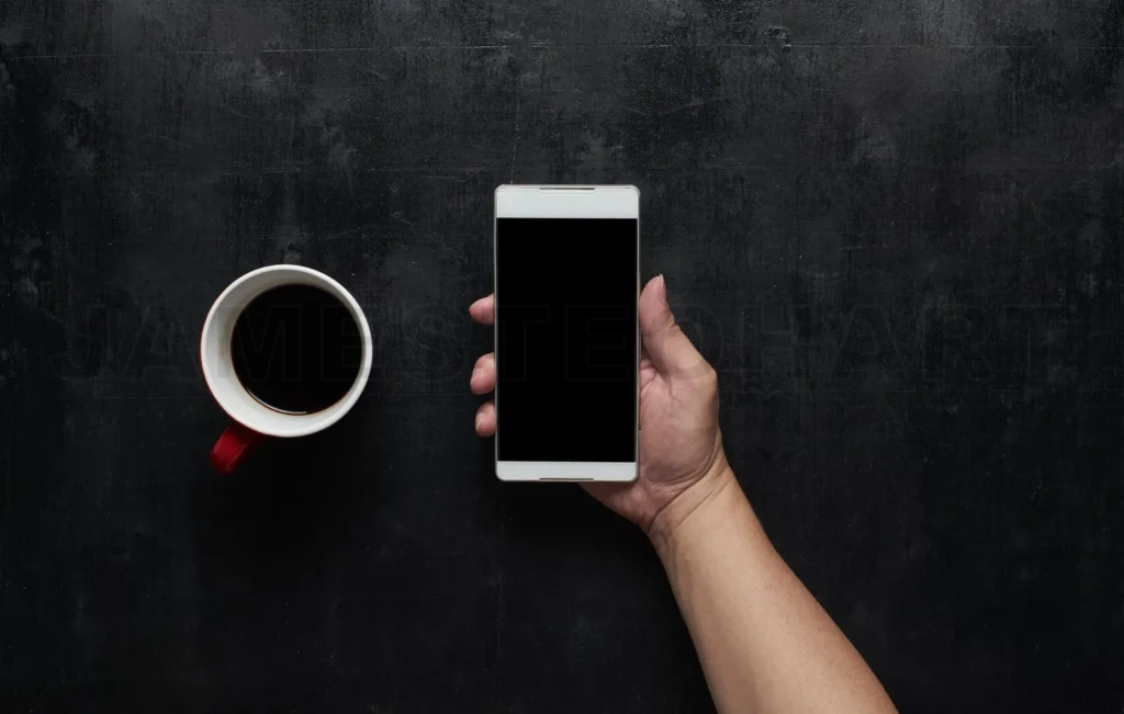 
Hand Holding Black Screen Smart Phone  With Cup Of Coffee