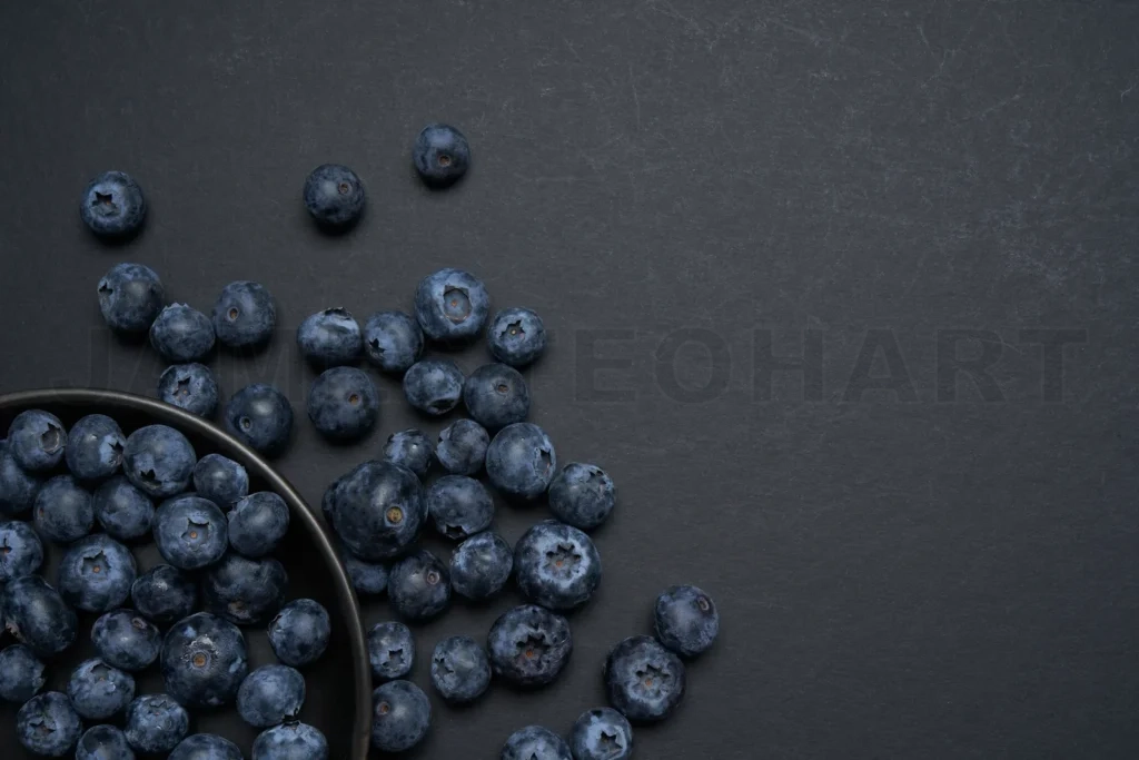
Fresh organic blueberries spilling from a bowl onto dark background