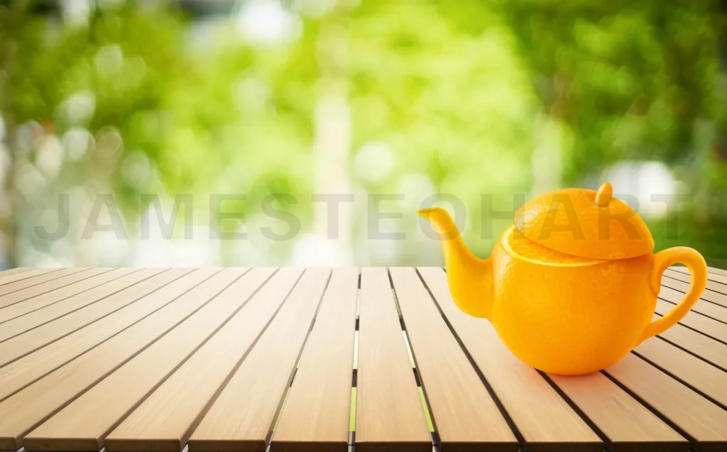 
Teapot Of Orange Fruit On Wooden Table With Out Of Focus Green Park Background