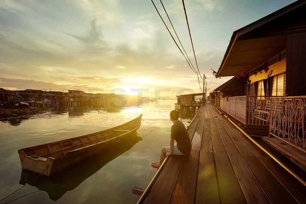 
Man watching sunset over wooden jetty in village