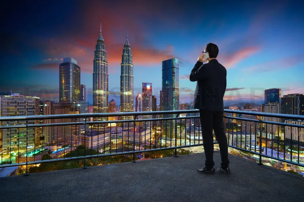 
Young Businessman Standing On A Balcony  Using Smartphone With Beautiful City Skyline Background
