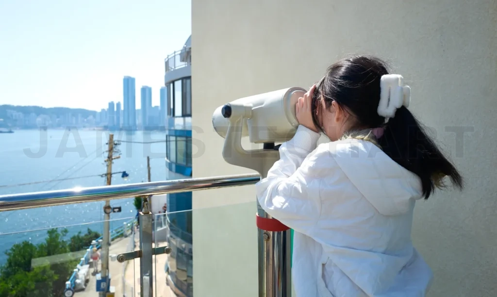
Young girl using binoculars to look at the cityscape of busan, s