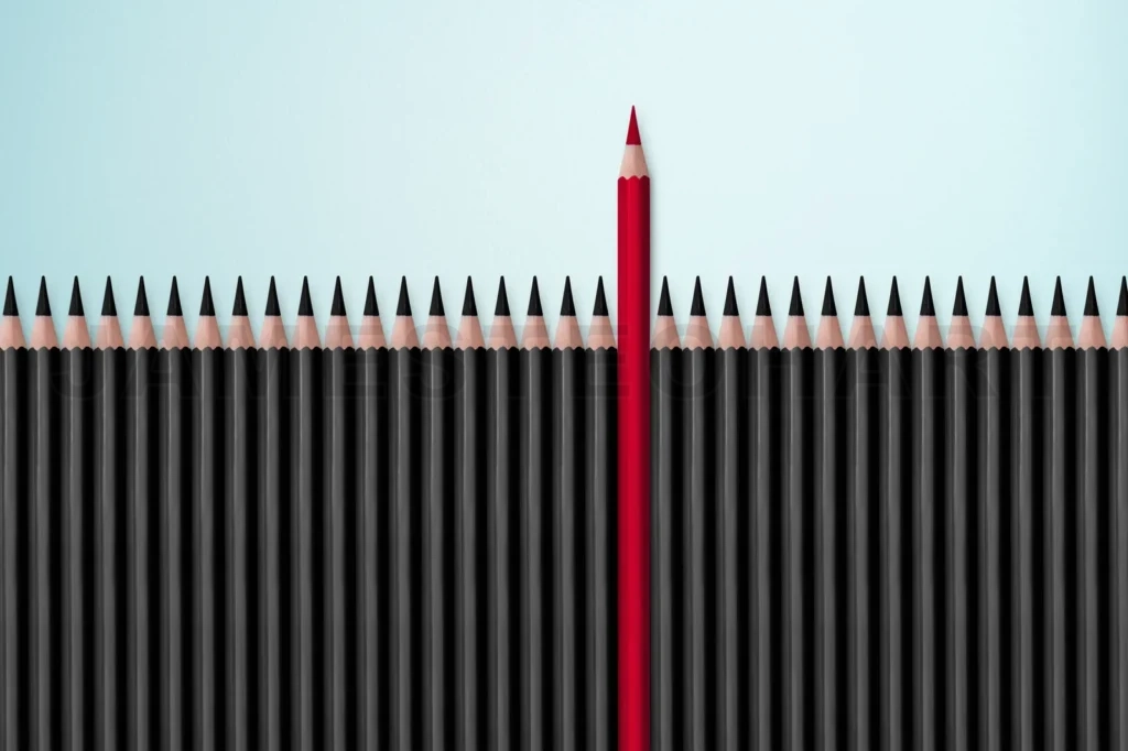
Red Pencil Standing Out From Crowd Of Plenty Identical Black Fellows On White Table
