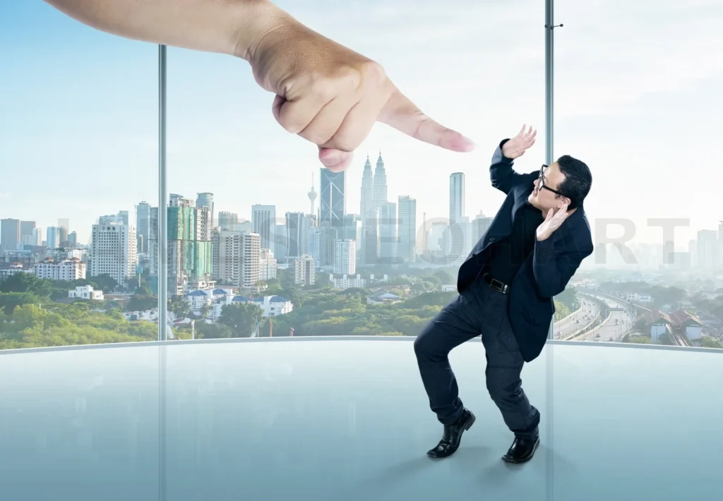 
A Scared Businessman Full-Height In A Scare Pose And A Giant Hand Pointing At Him, On The Office Background